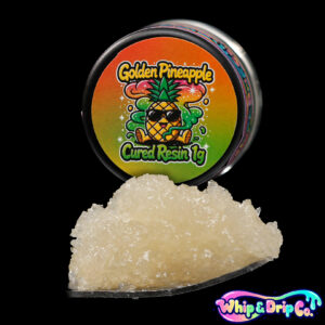 Whip & Drip Co. Golden Pineapple cured resin concentrate with pale golden extract displayed beside tropical pineapple-themed 1 gram product packaging on a black background.