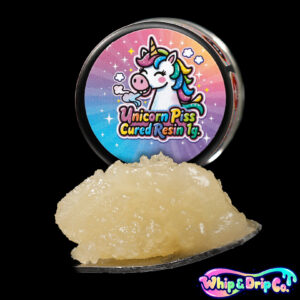 Whip & Drip Co. Unicorn Piss cured resin concentrate with pale golden extract displayed beside colourful unicorn-themed 1 gram product packaging on a black background.